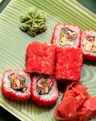 Red California Sushi roll in masago or tobiko caviar. Inside-out Japanese Sushi Set on green background. Bright colors. Healthy Oriental food. Soft focus. Vertical format. Closeup shot.