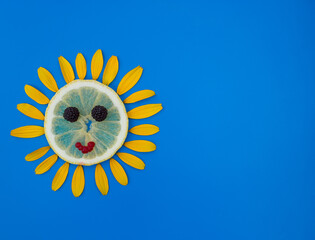 sun laid out from a slice of lemon and yellow flower petals around on a blue background. Summer joyful mood, flower fantasies, creative idea. a symbol of warmth and joy. Copy space