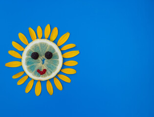 sun laid out from a slice of lemon and yellow flower petals around on a blue background. Summer...