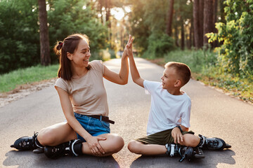 Outdoor shot of happy family mother and son wearing casual style clothing and roller skates sitting...