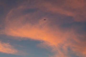 The sunset tinted the clouds in red tones. A flying plane can be seen against the background of pink clouds.
