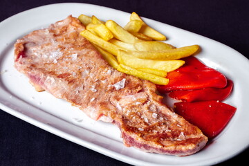 Beef steak with potatoes and peppers on white plate and on black background