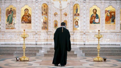 The Iconostasis inside an orthodox church. Video. Rear view of a priest standing in front of the icons with the faces of the saints, concept of religion, interior details inside a church.