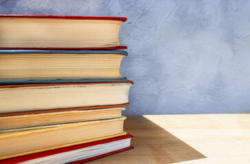 Stack of colorful hardback books on wooden table close up against gray and blue concrete wall
