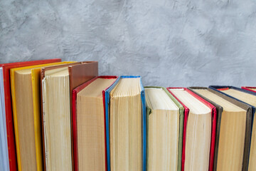 Row of multicolored hardback books on wooden table against gray and blue concrete wall