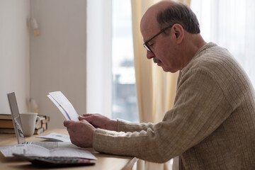 Senior man sitting at table at home alone with paperwork