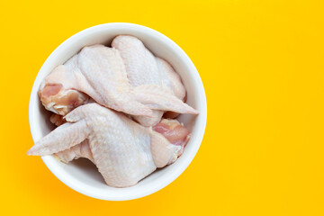 Fresh raw chicken wings in white bowl on yellow background.