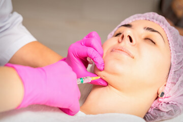 The cosmetologist makes lipolytic injection on the chin of a young woman against the double chin in...