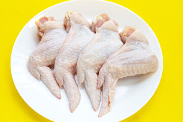 Fresh raw chicken wings in white platel on yellow background.