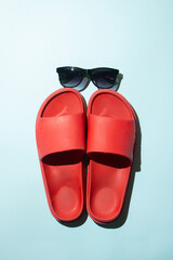 Black sunglasses with red beach slippers against pastel blue background. Flat lay. Minimal summer concept.
