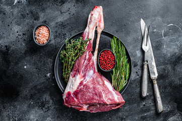 Raw goat or lamb leg meat on the bone with herbs. Black background. Top view. Copy space