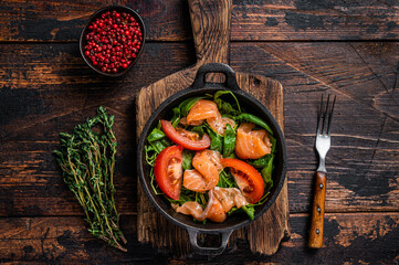 Fresh salmon salad with arugula, tomato and green vegetables. Dark wooden background. Top View