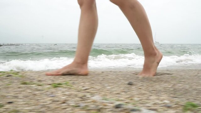 Women's feet walk on the sand near the sea with waves. High quality FullHD footage