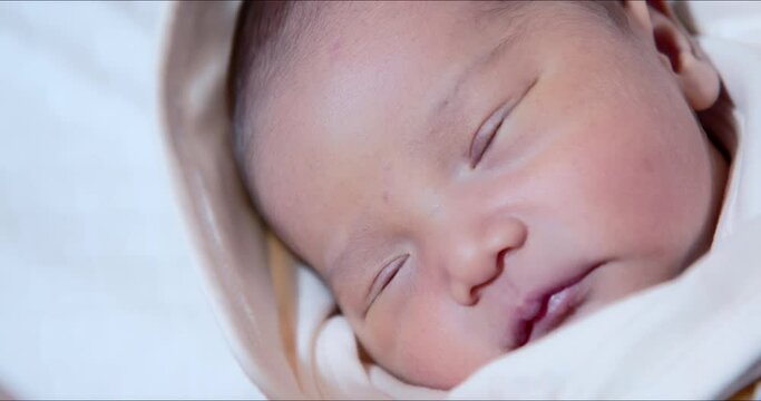 Asian newborn baby girl tries to open eyes extreme close-up shot. Adorable 0&ndash;6-month-old infant with closed eyes. Neonatal first days in life concept.