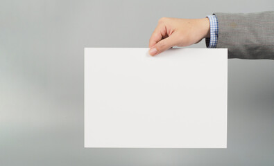 Hands is holding board white paper on gray background.Wear grey suit.businessman concept.