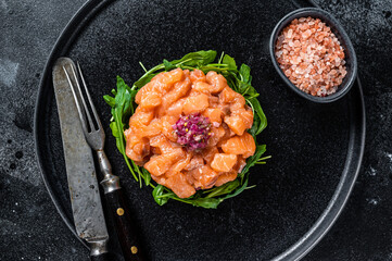 Raw Salmon tartare or tartar with red onion, arugula and capers in black plate. Black background. Top View