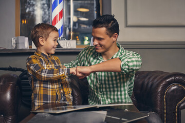 Young father and his stylish little son in the barbershop in the waiting room.