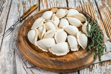 Fototapeta na wymiar Homemade raw frozen dumplings, vareniki, pierogi stuffed with potato on a wooden board. White wooden background. Top View