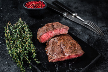Grilled Top Blade or flat iron roast beef meat steaks on marble board. Black background. Top View