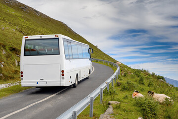 Small white tourist bus travelling on a small road in a beautiful mountains, blue cloudy sky....