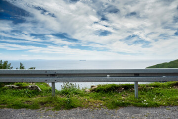 Metal barrier by a road, ocean and blue cloudy sky in the background. Road safety concept. Keem...