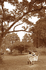 Sepia image of happy couple sitting side by side on a wooden swing in the garden