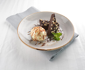 walnut chocolate brownie with vanilla ice cream and peanut, chocolate sauce, mint leaf dessert on round plate western pastry halal menu