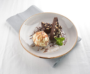 walnut chocolate brownie with vanilla ice cream and peanut, chocolate sauce, mint leaf dessert on round plate western pastry halal menu