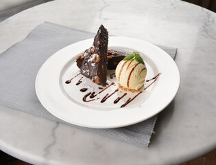 walnut chocolate brownie with vanilla ice cream and peanut, chocolate sauce, mint leaf dessert on round plate western pastry halal menu
