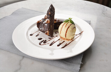 walnut chocolate brownie with vanilla ice cream and peanut, chocolate sauce, mint leaf dessert on round plate western pastry halal menu