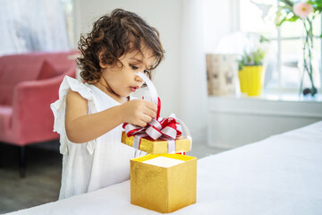Fototapeta na wymiar Portrait of adorable little girl opening birthday box gift and looking inside with surprised joyful facial expression