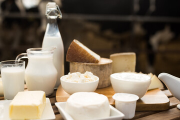 jug of milk, bottle of kefir, cottage cheese, cream and yogurt in bowl, cheese, butter on table in barn