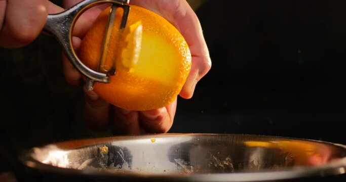 Male hands peeling orange fruit with special tool on black background. Close up shot in slow motion with RED camera.
