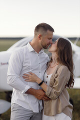 A couple of lovers, in the cockpit on their own plane. Smiling people and a private plane in the background.