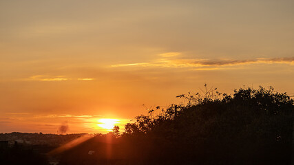 Sunset highlighted by the orange color, with dramatic clouds, below the horizon and in the right corner the silhouette of a tree
