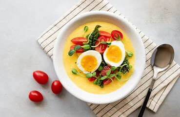 polenta bowl with fresh vegetables, microgreens and eggs on gray table. Healthy balanced breakfast or lunch. top view