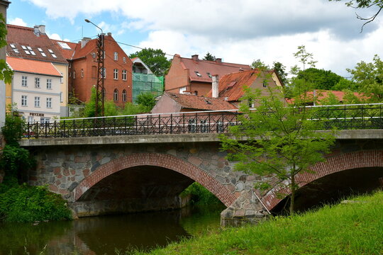 A view of an old abandoned historic buildings with some modern extensions standing in the middle of an old city next to a medieval bridge made out of stone and metal spotted on a Polish countryside