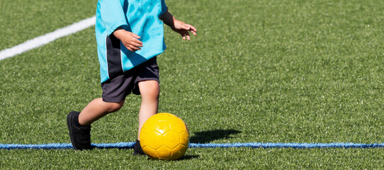 Young child dribbleing a yellow soccer ball on a turf field