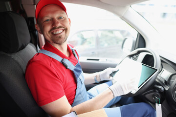 Man courier sitting behind wheel of car and holding digital tablet in his hands