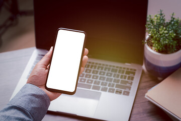 mockup image smartphone blank screen for hand typing text,using laptop contact business searching information in workplace on desk at office.design creative work space vintage tone concept.