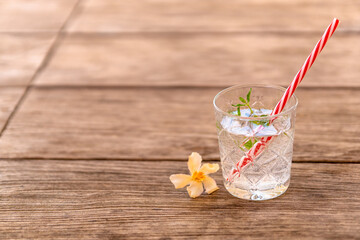 Refreshing summer drink with a straw. Cold cocktail with gin and lemonade garnished with fresh mint and an oleander blossom on a wooden table. Background with copy space.
