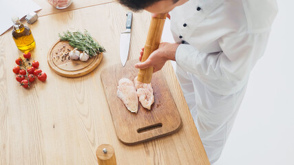 High angle view of chef seasoning chicken fillet on chopping board