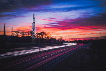 Space and Rocket Center with Long Exposure Light Trails from Cars with Sunset in the Background - obrazy, fototapety, plakaty