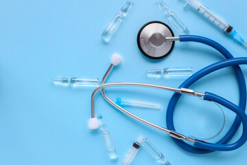 Top view of medical supplies - stethoscope, syringe and vaccine ampoule on blue background