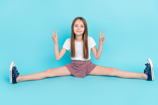 Full size photo of cool brown hair small girl stretch show v-sign wear white t-shirt skirt isolated on blue color background