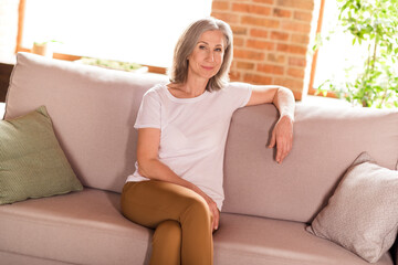 Photo of charming sweet old woman dressed white t-shirt sitting sofa smiling indoors flat home house