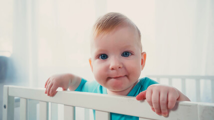 baby boy with blue eyes looking at camera from white crib