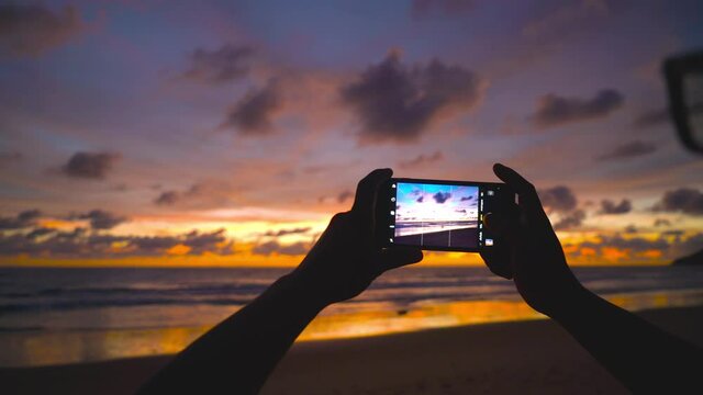 Travel video. Close-up screen smart phone take a photo and video sunset on beach Travel on vacation at a beach and sunset time.  The most beautiful sunset of the sea in summer sun in Phuket, Thailand.