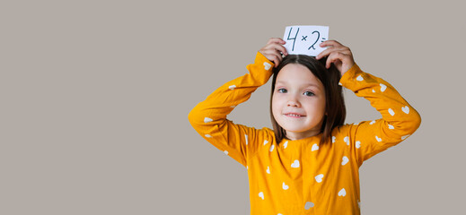 funny crazy cute kid girl in mustard dress learns the multiplication table on beige background,...