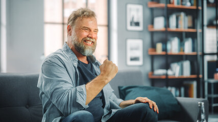 Charismatic Bearded Man Sitting on a Couch Watches Game on TV, Celebrates Sports when Team Wins...